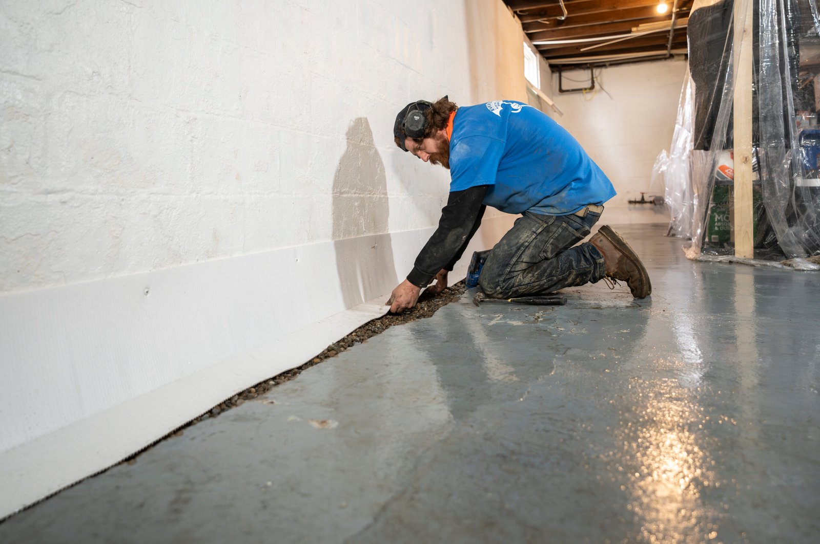Waterproofing specialist inspecting basement wall seepage with moisture meter and protective equipment