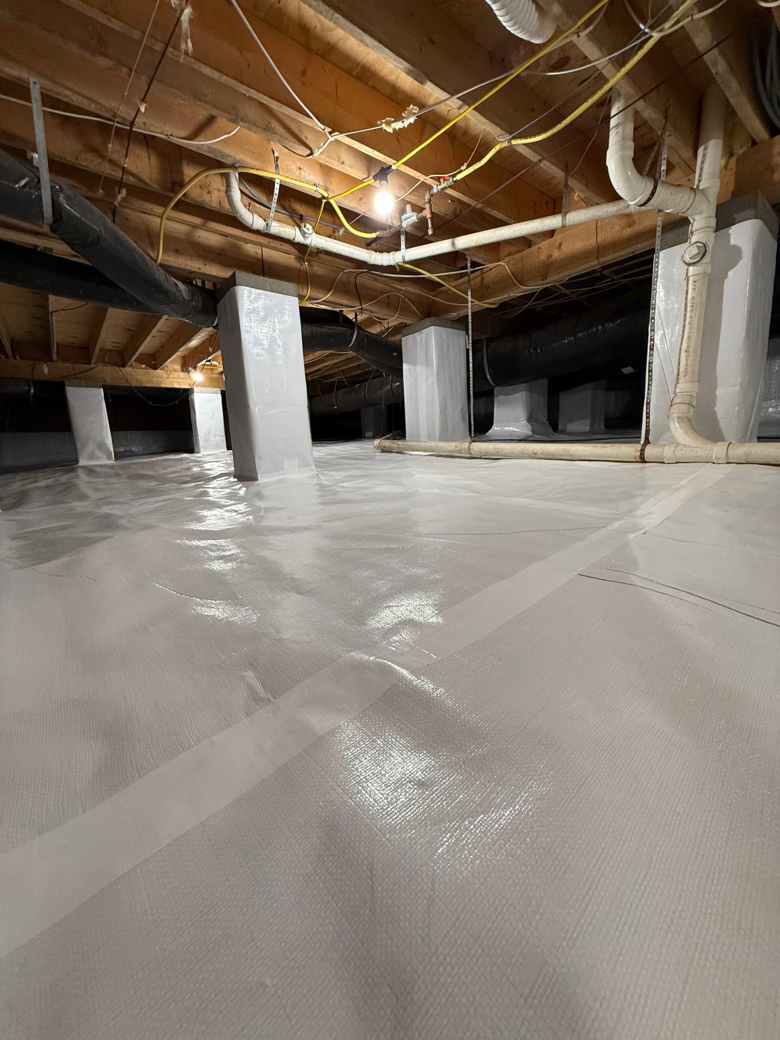 Specialist inspecting crawlspace drainage and moisture barriers with professional lighting and tools