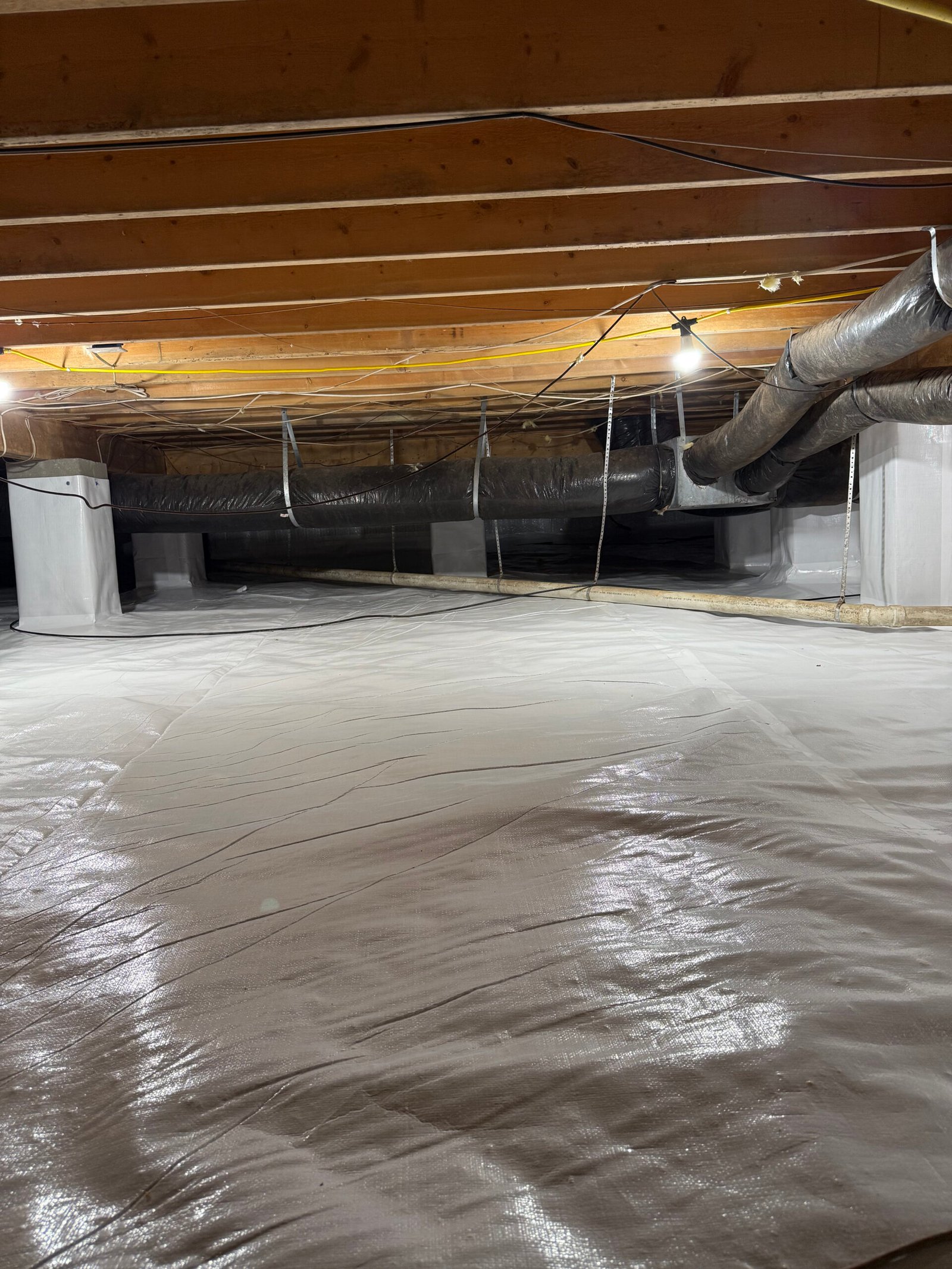 Technician installing vapor barrier in damp crawlspace beneath Central North Carolina home after rainfall