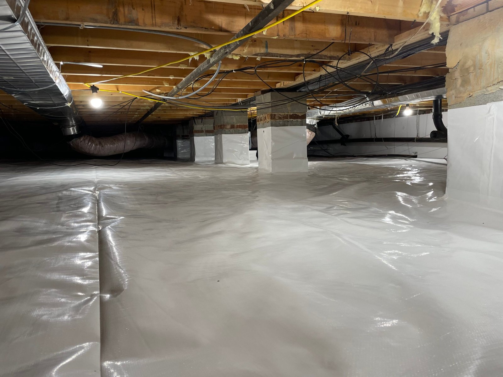 Specialist inspecting crawlspace drainage and moisture barriers with professional lighting and tools