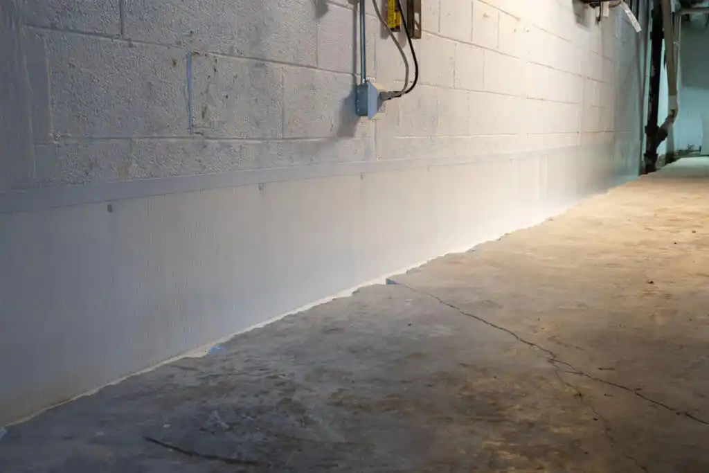Waterproofing specialist inspecting basement wall seepage with moisture meter and protective equipment